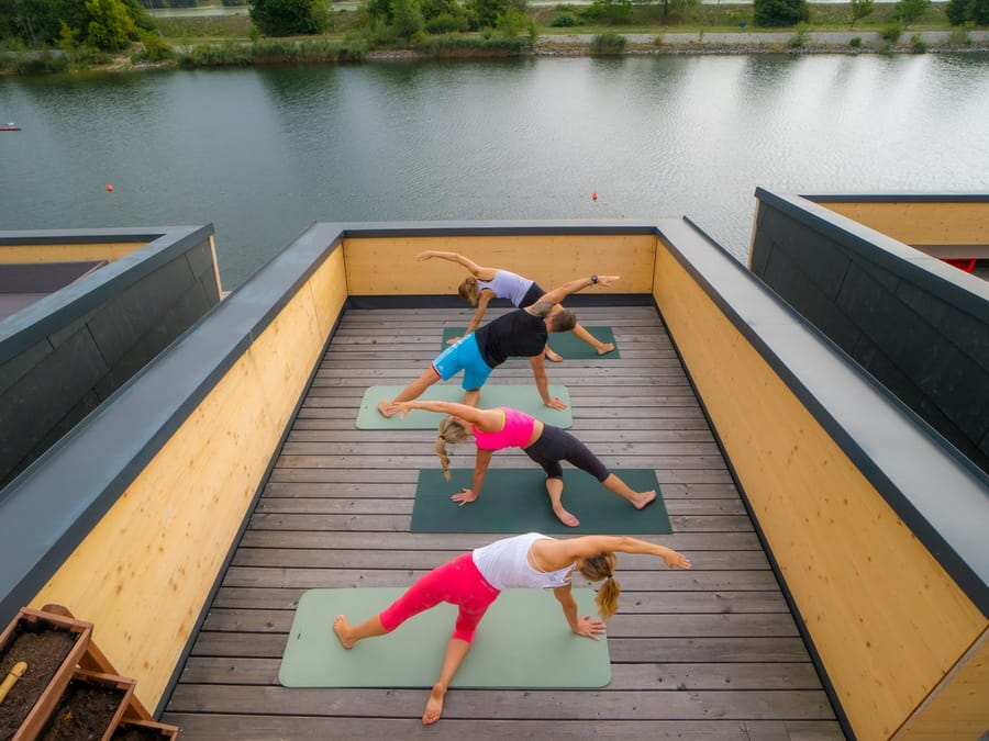 Ahşap bir terasta yan yana serilmiş matlarda mat pilates çalışması